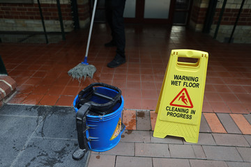 Cleaning in progress sign with male cleaner cleaning rinsing his mop in the blue bucket beside  - obrazy, fototapety, plakaty