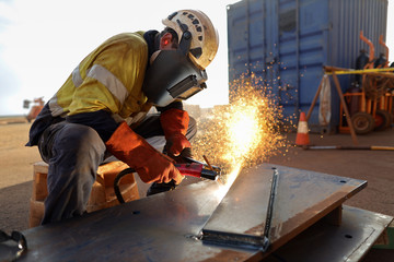 Construction worker wearing safety ears plug  helmet, face shield, red welding leather glove protection while commencing hot work gouging metal plate on the ground surface   
