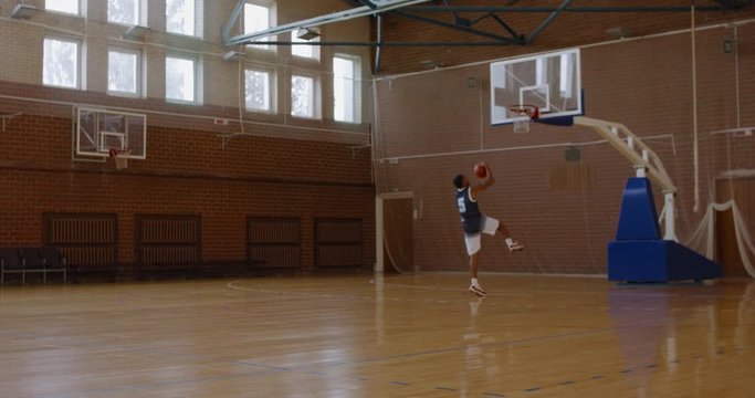 WIDE African American black college male basketball player practicing dunks alone on the indoor court. 4K UHD 120 FPS SLOW MOTION RAW Graded footage