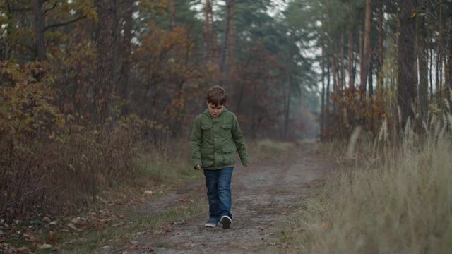 Kid in jacket coming by fall forest path in slow motion. Face of child approaching to camera. 