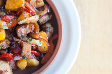 Roasted pork with steamed vegetables: potato, onion, bell pepper in the ceramic plate. Caucasian georgian food ojahuri. Horizontal top view from above.