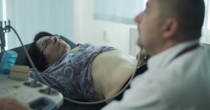 Male doctor specialist examining senior female patient on bed with ultrasound machine in the office room.
