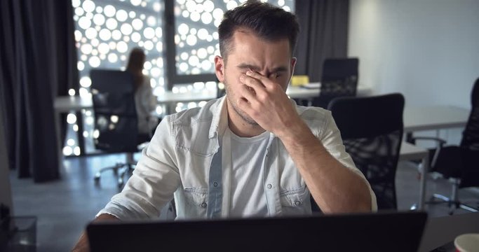 Exhausted male office employee massaging eyes while working on laptop in office, harm for health, risk pf poor vision