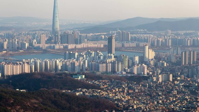 Timelapse modern Seoul buildings surround blue river and Lotte World Tower against hill silhouettes in morning pan up