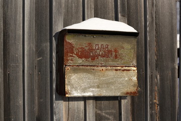 Old metal mailbox for letters. The inscription on the box is "for letters". Mail box in winter under snow on a wooden wall of a fence street outdoor