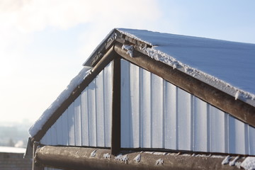 Snowy slope of a metal roof. Triangular end face of the roof in a winter day. Part of the building