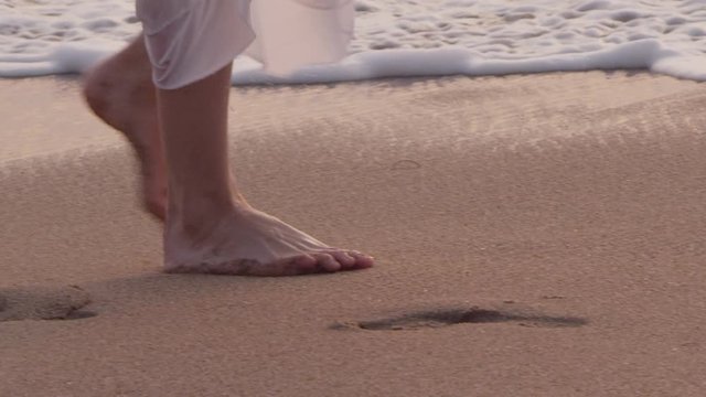 Close-up of a woman’s feet walking through beach sand at sunset