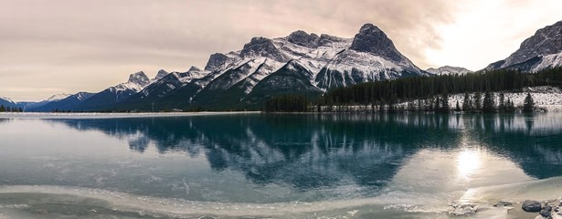 Wide Panoramic Winter Landscape of Frozen Mountain Lake and Rugged Snowcapped Peaks above Canmore, Alberta in Canadian Rockies near Banff National park