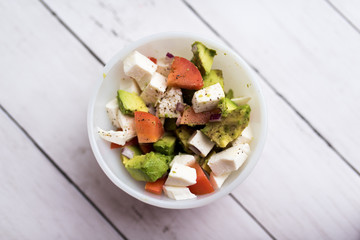 healthy salad from fresh vegetables with avocado, tomatoes and fresh mozzarella cheese served in white bowl