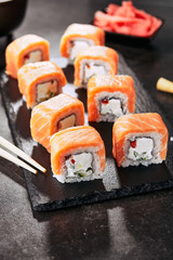 Beautiful Philadelphia Sushi Rolls Set with Salmon and Cream Cheese and Cuccumber on Black Slate Plate Close Up. Uramaki, Nori Maki or Futomaki Sushi with Trout Fillets, Soy Sauce and Wasabi