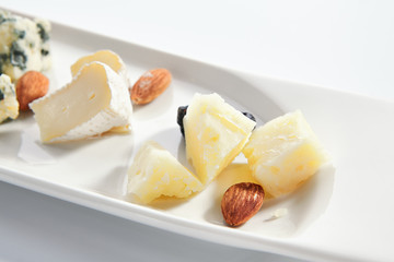 Cheese assorti platter closeup. Gorgonzola, brie, parmesan and chevre slices. Cow and goat milk chopped cheese on plate. Served delicious snacks composition isolated on white background