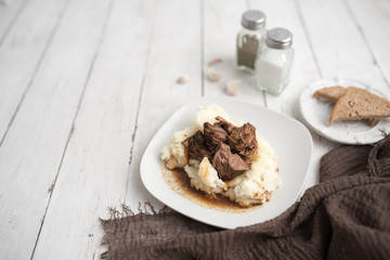 Beef tips with gravy on mashed potatoes served on white plate