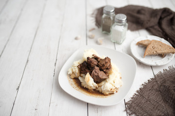 Beef tips with gravy on mashed potatoes served on white plate