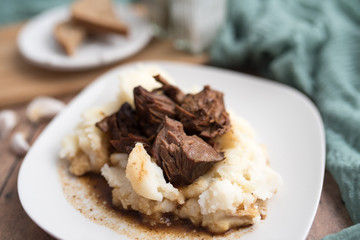 Beef tips with gravy on mashed potatoes served on white plate