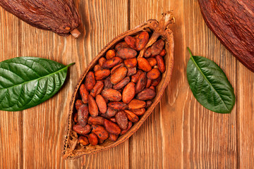 Cocoa beans and cacao pods with natural green leaves on a wooden background. Top view. Text space.