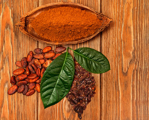 Cocoa pod with cacao powder, cocoa butter, green leaves, two leaves made of cocoa beans and cacao nibs on wooden background. Top view.