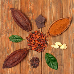 Cocoa pods with green leaves, chopped chocolate bar, cocoa butter, cacao powder, heaps of cocoa beans and cocoa nibs on wooden background. Top view.