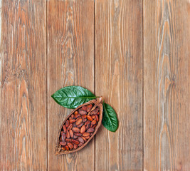 Cocoa beans in cacao pod with natural green leaves on old wooden background. Top view. Text space.