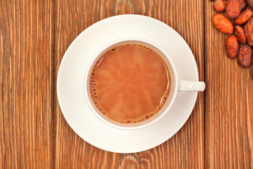 Cup of cacao drink with cocoa beans on wooden background. Top view.