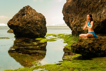 Young woman sitting on the rock, meditating, practicing yoga and pranayama at the beach, Bali....