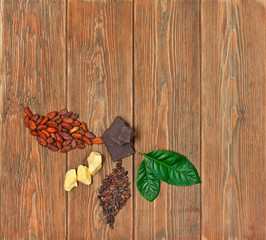 Two leaves made of cocoa beans and cacao nibs, chopped chocolate, cocoa butter and green leaves on wooden background. Top view. Text space.