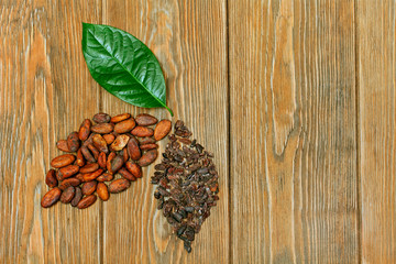 Green leaf and two leaves made of cocoa beans and cacao nibs on wooden background. Top view. Text space. Ecology concept.