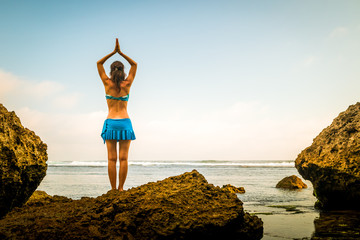 Woman standing on the rock, practicing yoga. Young woman raising arms with namaste mudra at the...