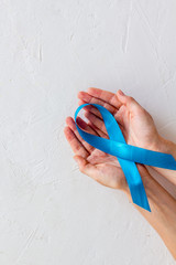 Blue ribbon in hands as symbol disease control on white background top view copy space