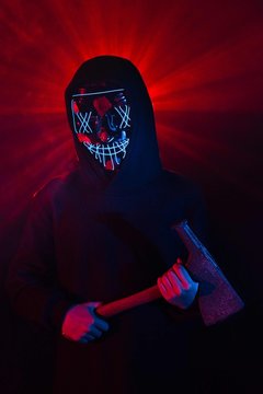 A person wears an illuminated mask for halloween and adds props to increase the effect of the costume 