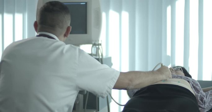 Doctor internist and senior female patient during medical examination on ultrasound machine.