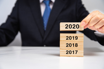 Hand of businessman stacking wooden blocks on the table in 2020.