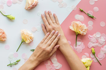 Obraz na płótnie Canvas Stylish trendy female pink manicure. Beautiful young woman hands on pink and white background with flowers and place for text. Minimal creative concept. Flat lay, top view, mock up copy space template