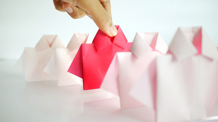 Hand selecting one Red among white origami shirt paper , unique individuality and difference or...