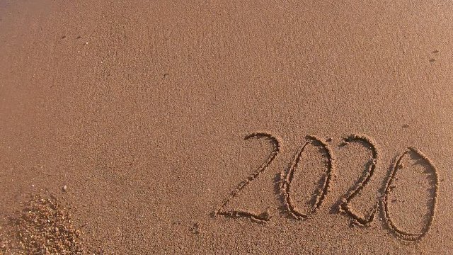 The wave washes away the numbers 2020 in the sand.Happy New Year 2020 is coming. New Year 2020 is coming concept - figures on a sand beach.