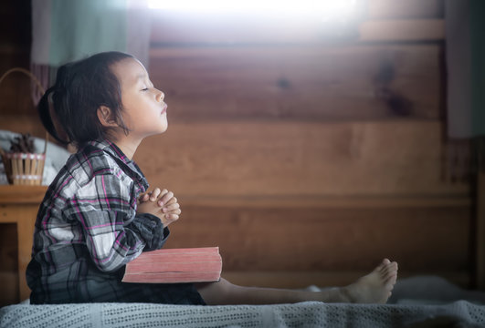 asian little girl reading and praying on Bible in morning at home. christian concept.