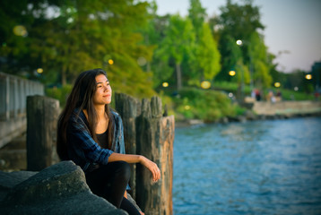 Biracial teen girl  sitting  looking out over lake at sunset - Powered by Adobe