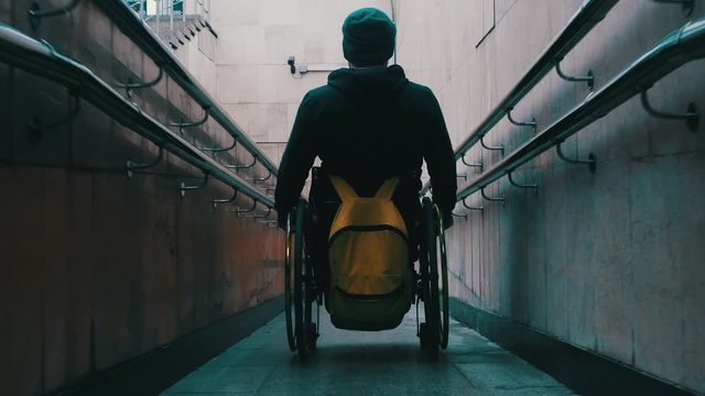 Disabled man in wheelchair getting down the long ramp in the subway