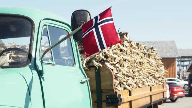 Cinematic footage. Norwegian flag waving in the wind on a background of a truck loaded with dried cod. Symbol of Lofoten Islands, Norway.