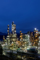 Fototapeta na wymiar Vancouver oil refinery with night illumination against the blue sky and mountain range