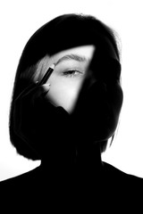 Portrait of a girl on a white background. Fashion model uses cosmetic pencil for eyebrows and eyelids. Black-white.