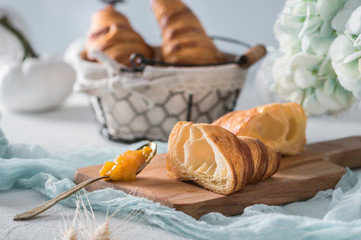 Freshly baked croissants with orange jam on light background