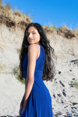 Beautiful model looking  at camera at the beach in Sligo in Ireland. Mixed race Portuguese Indian female model posing. Blue dress.  Black hair model. Irish coastline.