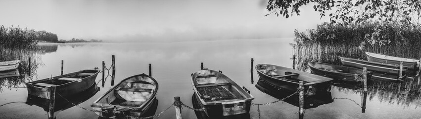 on a lake some rowboats are moored and on the lake there is fog and the lake is quite calm