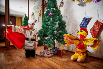 Two brothers in carnival costumes at Christmas or new year at the Christmas tree in the room. Little boys indoor