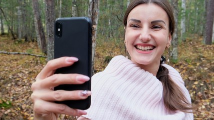 laughing female in autumn forest talking on phone on skype.