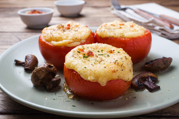 Baked whole tomatoes stuffed with mushrooms and cheese with seasonings on a wooden background. Close up Selective focus