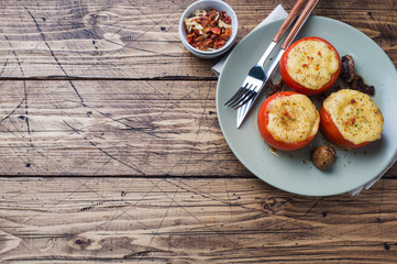 Baked whole tomatoes stuffed with mushrooms and cheese with seasonings on a wooden background. Copy space.