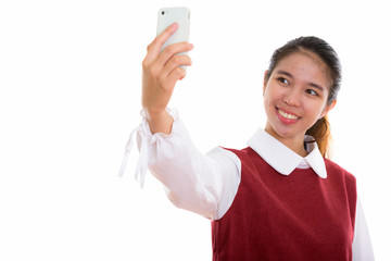 Studio shot of young happy Asian woman using phone