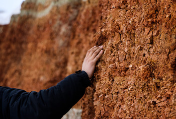 young man walks in  clay career in winter.  guy touches his hands with multi-colored layers of clay in  excavation.