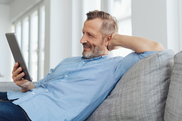 Happy man relaxing at home with a tablet